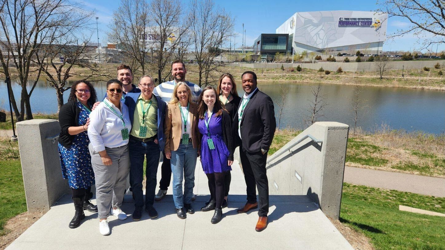 A group of Michigan LCV staff and board members posing for a photo in front of a river. The group is all dressed in business formal attire. 